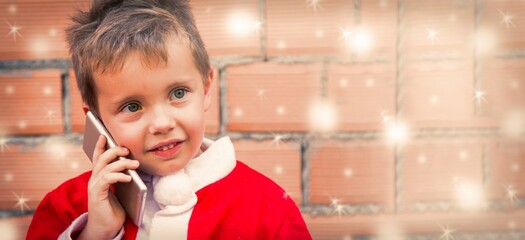 smiling boy in santa claus costume talking with mobile phone