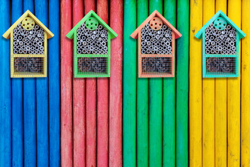 Colorful wooden houses for insects hanging on multicolored wooden fence.