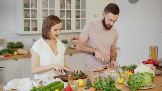Young couple cooking together preparing dinner chopping vegetables and talking at home 