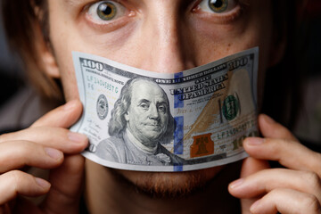 Man covers his mouth with a $100 bill