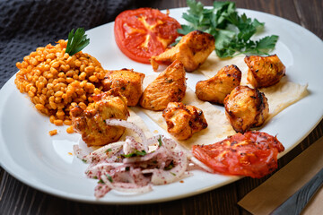 Light and delicious grilled chicken kebab, located on a platter with tomato and bulgur, decorated with cilantro sprigs. Healthy and tasty oriental cuisine. Close-up, shallow depth of field