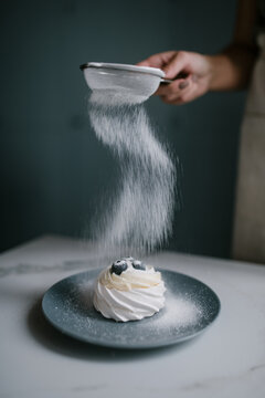 Woman pouring powdered sugar on pavlova cake