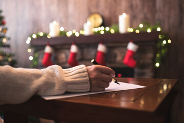 Hand of young woman with fountain pen and sheet of paper on background of christmas tree and...