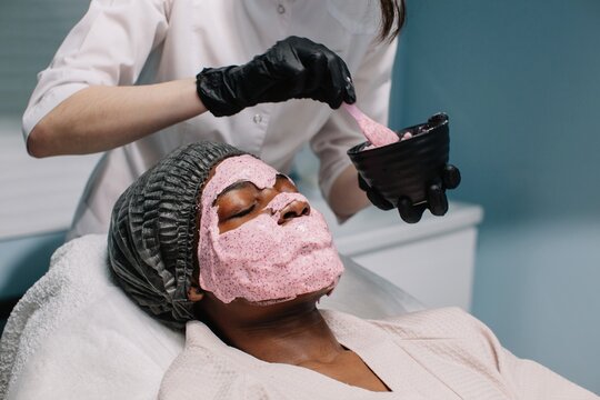 Cosmetician apply pink alginate mask on client's face