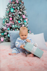 Fototapeta na wymiar baby boy in a striped jumpsuit sits and opens a gift on the background of a Christmas tree. Vertical orientation