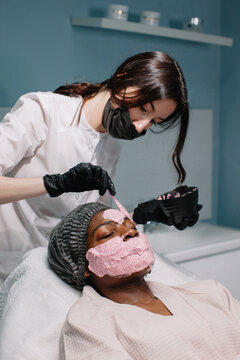 Cosmetician apply pink alginate mask on client;s face