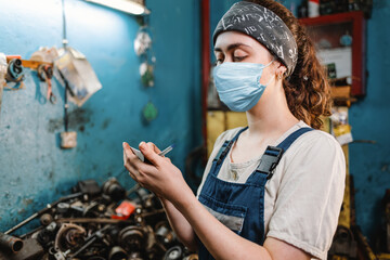Gender equality. Portrait of a young woman in uniform, working in a workshop, which writes down orders on a piece of paper. In the background is a blue wall and a table with spare parts. Close up