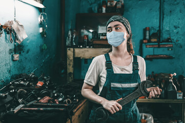 The concept of small business, feminism and women's equality. A young woman in overalls holds a large wrench and looks away