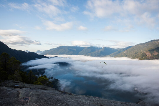 A paraglider flying over a foggy mountain valley on the BC coast