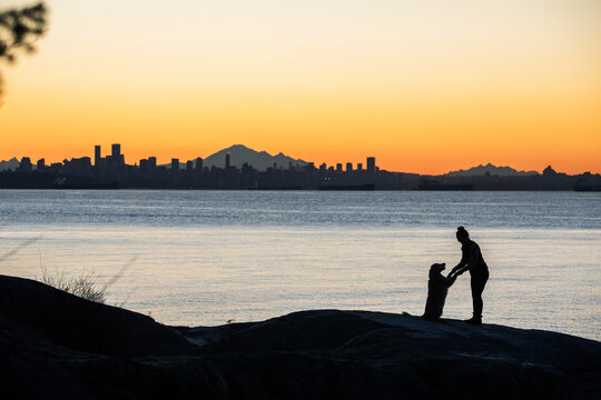 Young woman and her dog overlooking sunrise over Vancouver, BC.