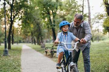 boy teaching to ride bike with his grandfather in public park