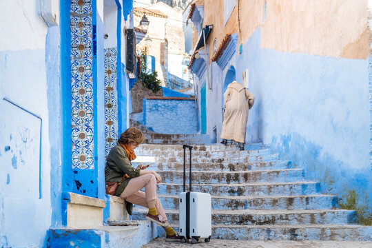 Female sitting with suitcase in blue town