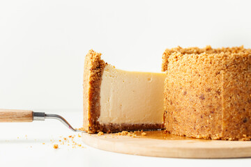 Homemade classic New York cheesecake cut on the wooden board. Vanilla pie with cheese and crunchy crust on the whiite background. Close up, macro shot