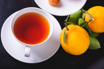 White glass cup with black, red tea with lemon on a dark glass table.