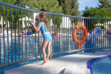 A girl is wearing light blue and rose swimsuit stands at the swimming pool