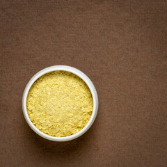 nutritional organic yeast flakes in a small ceramic bowl against handmade textured paper with a copy space, nutrition supplement, baking and cooking