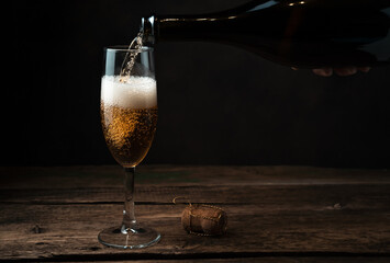 Glass in the process of filling with champagne with foam and bubbles on a wooden background. Side...