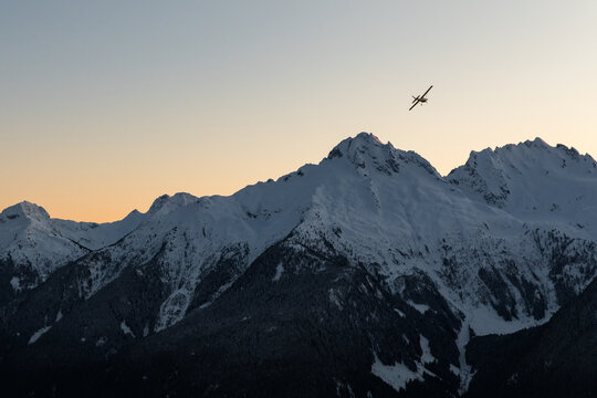 A single engine airplane flying through snowy mountains at sunset