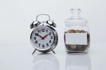 Fotobehang Coins in a glass bank with space for text and alarm clock in a white room. Deposit and growing concept. © burdun