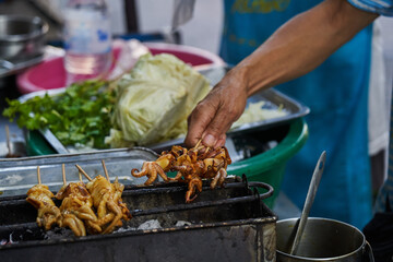 Crop man taking skewers with grilled octopus