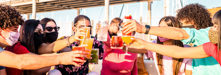 Group of happy friends with face mask drinking and toasting coloured cocktail at bar restaurant -...