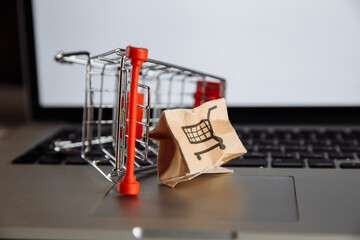 Damaged paper box and shopping cart on a keyboard of laptop. Cheap parcel delivery, poor shipment...