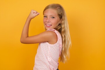Beautiful Caucasian young girl standing against yellow background,  showing muscles after workout....