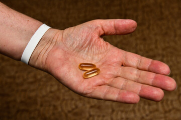 An elderly man holds vitamin D and fish oil, Omega capsules in his hands