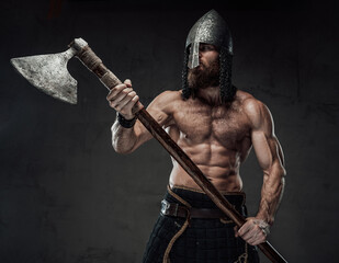 Furious and muscular nord warrior standing in dark background with naked torso and with his two...