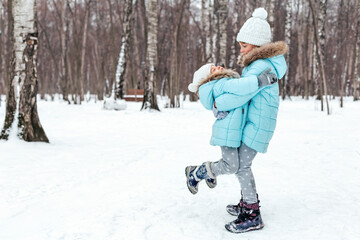 Fototapeta na wymiar Little girls, sisters are walking, having fun in snowy winter park. Stylish clothes, blue jackets with fur,warm pants with snowflakes,cat-shaped mittens.Family picnic in cold weather.Outdoor activity