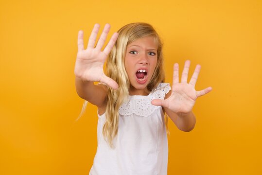 Dissatisfied Beautiful Caucasian young girl standing against yellow background frowns face, has disgusting expression, shows tongue, expresses non compliance, irritated with somebody.