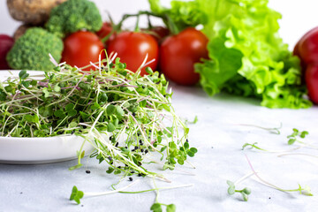 A white plate with fresh micro greens is on a white plate with green and red vegetable