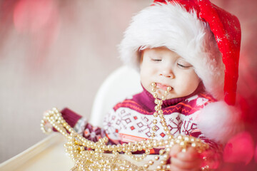 A little baby girl in a New Year's hat of Santa Claus examines and plays with New Year's decorations.
