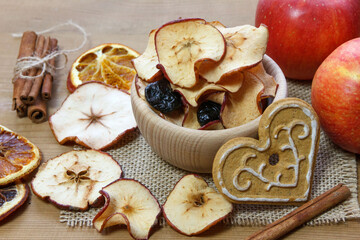 Dried apples and plums in a wooden bowl surrounded by cinnamon sticks, fresh apples and dried oranges