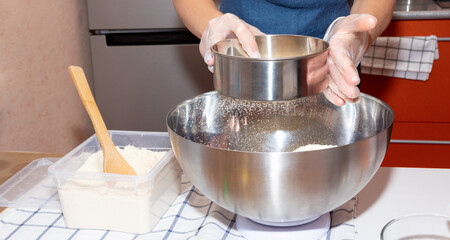 Sifting flour with a sieve into a metal bowl.