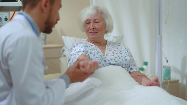 Caucasian Old Beautiful Woman Recovering Talking To Younger Professional Doctor Checking Pulse Communicating Giving Diagnosis. Medical Report. Elderly Patient. Healthcare.