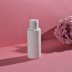 White cream tubes on the pink background  with pink peony and shadows. Summer vacation cosmetics concept. Top view. Selected focus