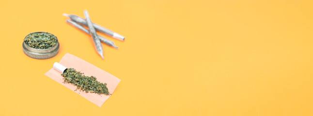 Joint of marijuana ready to roll and grinder full of weed on orange background.