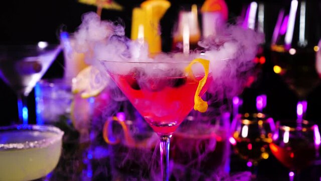 Cosmopolitan drink with cranberries at bar counter close up. Bartender show and prepared cocktail with dry ice on a cocktail bar background. Colorful various drinks in a bar with dry ice smoke effect.