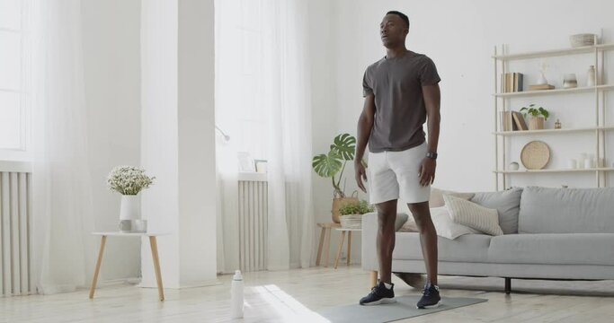 Home workout. Young sporty african american man doing squats exercises, sports training alone