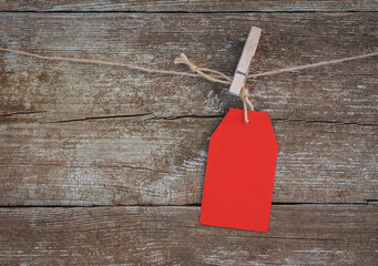 blank red paper tag held on a clothespin on a rope against a rustic wooden background