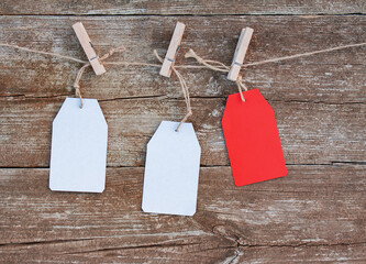 blank white and red paper tags attached with wooden clothespins to rope on rustic wooden background