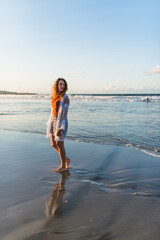 Young woman walking on a beach at low tide at sunset.