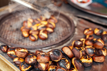 Costermonger roasting sweet chestnuts with tongs on counter. Famous traditional Turkish fried chestnuts on the counter of street seller.