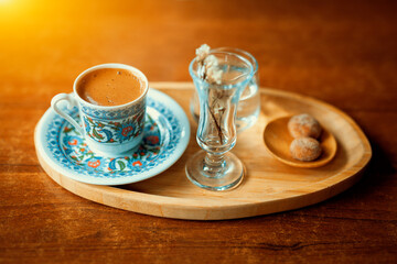 Traditional sparkling turkish coffee served with porcelain cup, cookies, glass of water and flower.