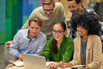 Group of happy multiracial business people sitting at desk in the modern coworking space, looking...