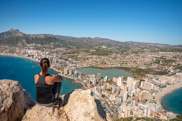 Fototapeta na wymiar Woman resting on top of the Peñon de Ifach, in Calpe, with views of the town of Calpe and the Mediterranean Sea.