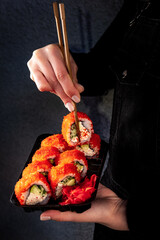 Woman eating delivered at home sushi from a container with japanese sticks
