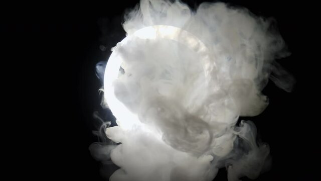 Smoke in slow motion passes through the circle of light on black background. White fog slowly floating, footage for logo