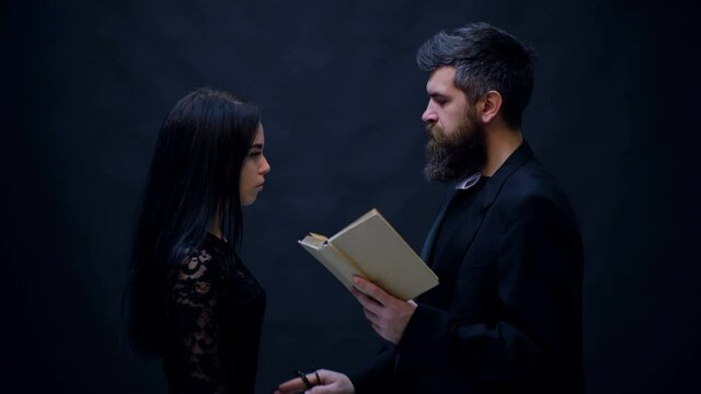 Young woman with pastor. Priest and prayer woman in the kneels. Girl is praying preaching priest with a prayer book isolated on black. Halloween party and celebration concept.